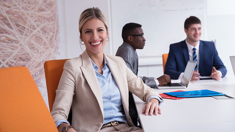 woman smiling at conference table with two other people behind her